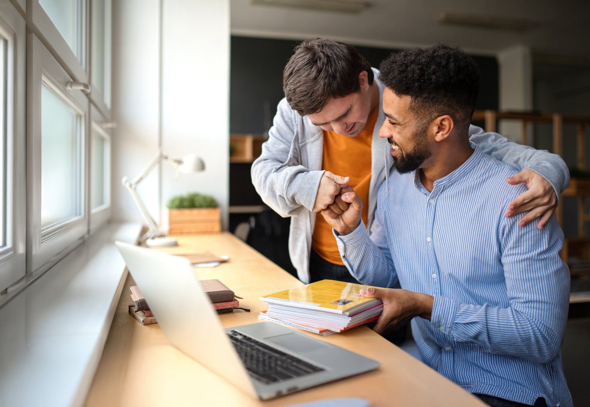 Happy young man with down syndrome fist bumping his aide